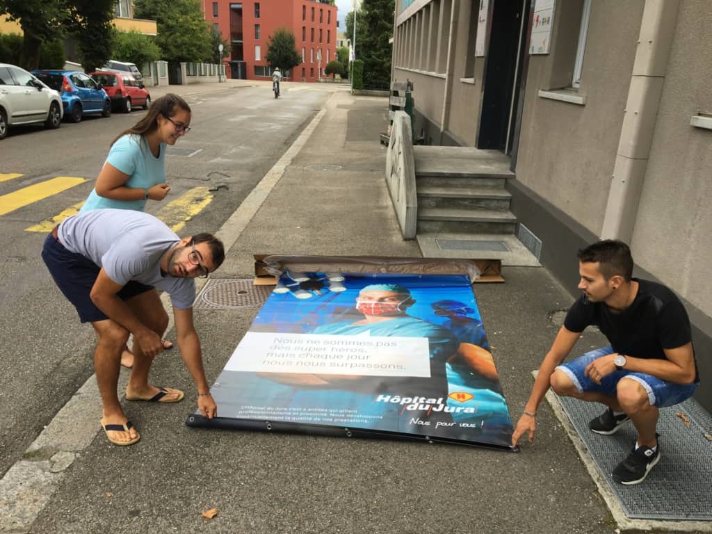 Plusieurs employés de chez Pomzed qui tiennent une affiche de l'hôpital du Jura.