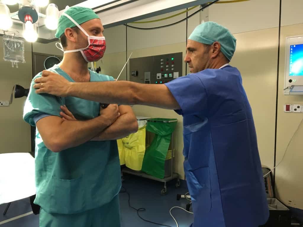 Dans la salle d'opération on voit un médecin tenir les épaules d'un autre médecin.